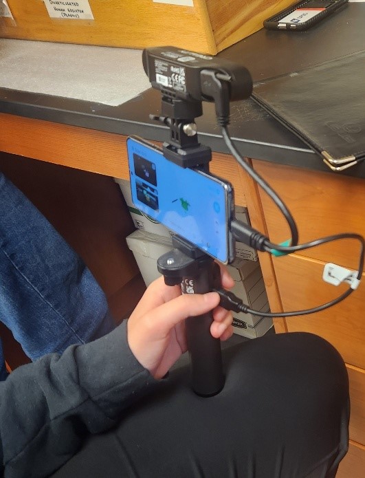 A closeup of a person's hand holding a handle attached to a smart phone.