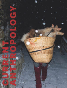A person walking in the snow caring a basket filled with an animal carcass.